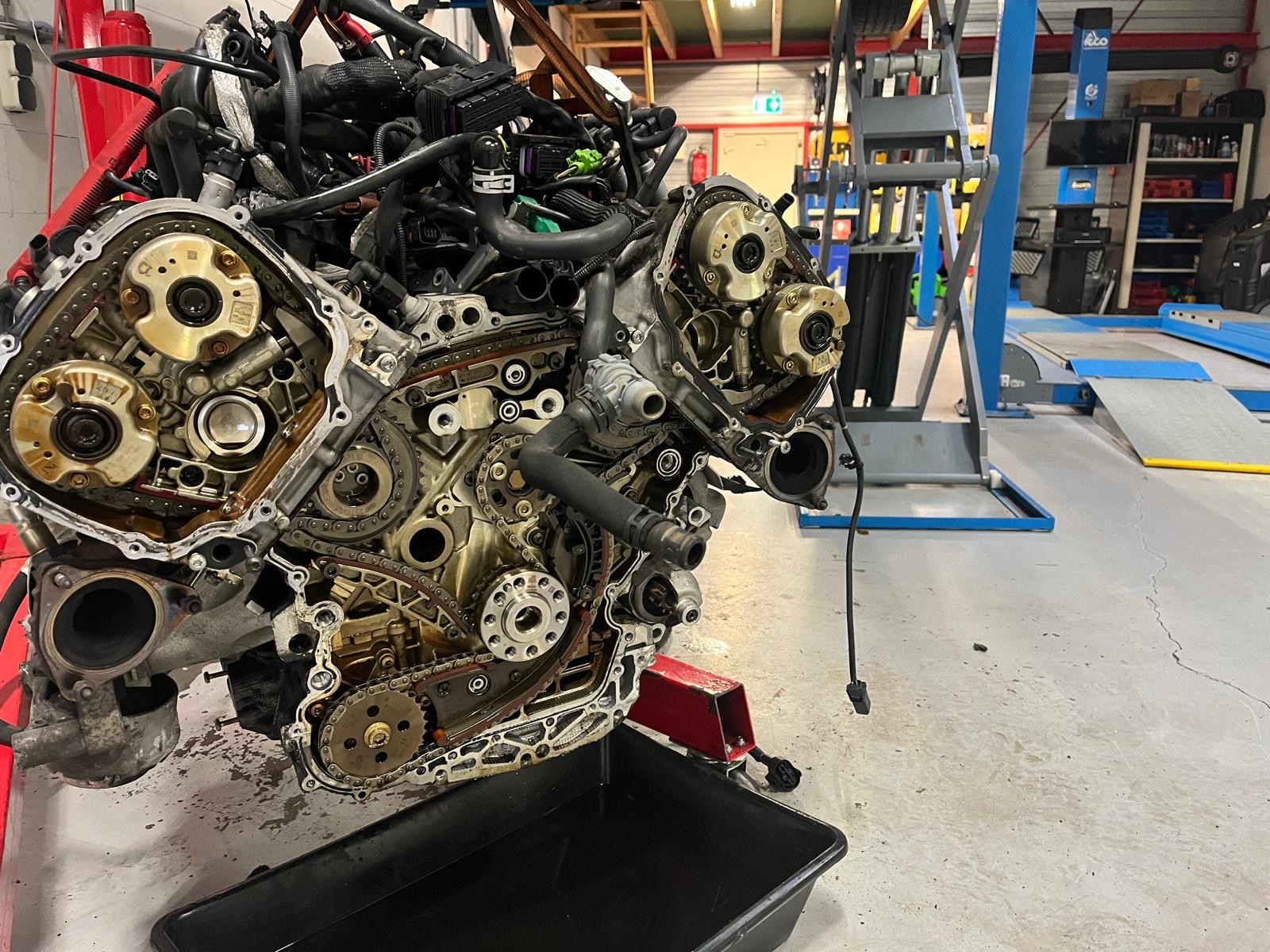 Gedemonteerde motor met distributieketting boven een oliebak