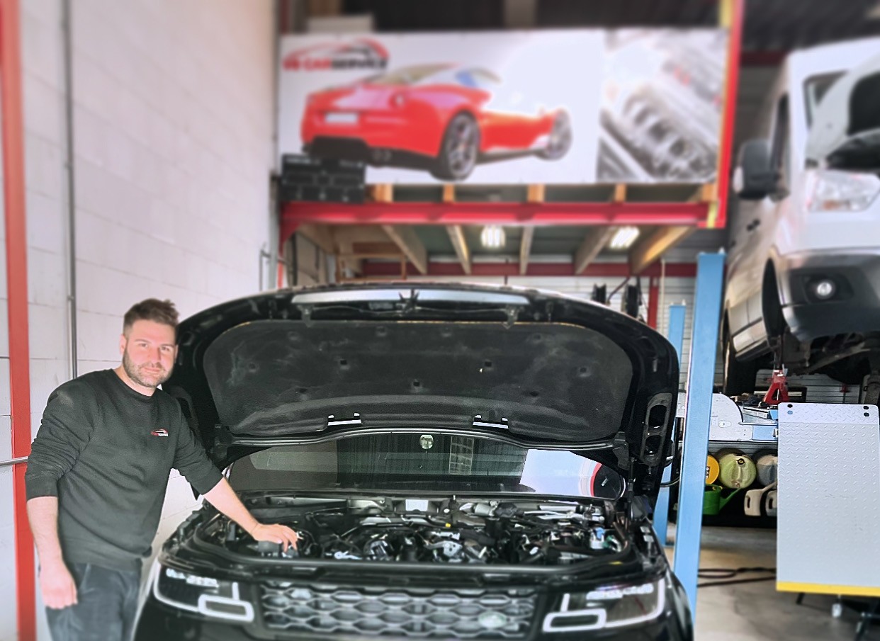 De monteur van V8 Car Service naast een Range Rover met open motorkap in de werkplaats